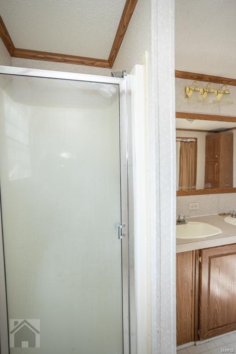 bathroom with a textured ceiling, vanity, ornamental molding, and a shower with door