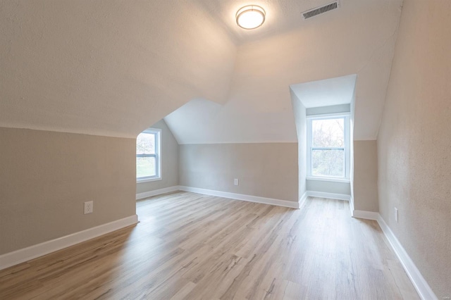 bonus room with a textured ceiling, light wood-type flooring, and lofted ceiling