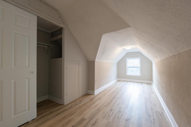 additional living space featuring a textured ceiling, light wood-type flooring, and lofted ceiling