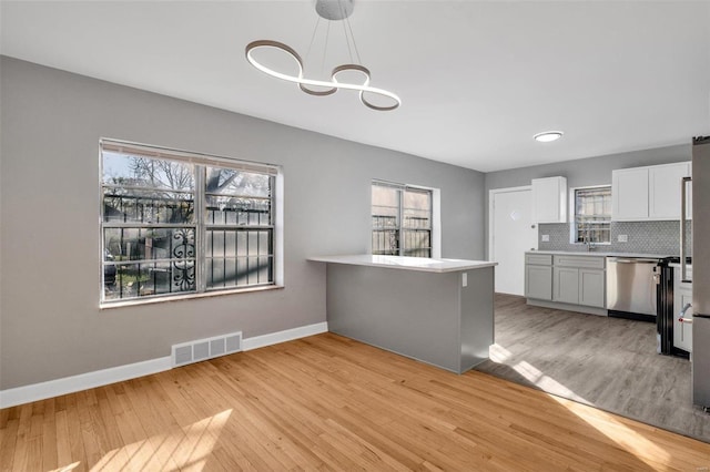 kitchen with white cabinets, hanging light fixtures, light hardwood / wood-style flooring, stainless steel dishwasher, and kitchen peninsula