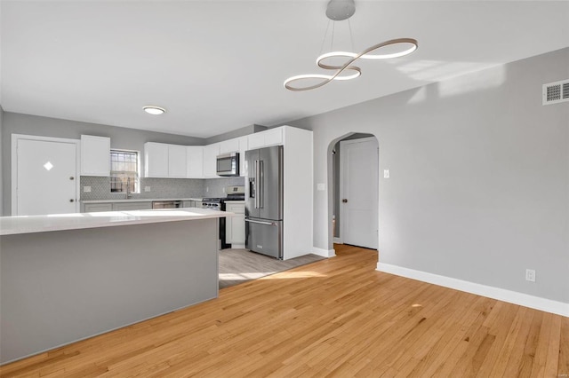 kitchen featuring light wood-type flooring, tasteful backsplash, stainless steel appliances, decorative light fixtures, and white cabinets