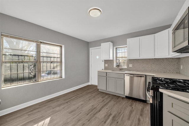 kitchen with white cabinetry, sink, backsplash, light hardwood / wood-style floors, and appliances with stainless steel finishes