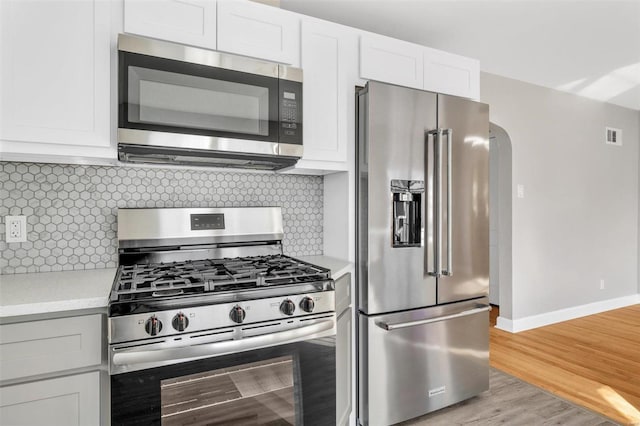 kitchen with white cabinets, light wood-type flooring, stainless steel appliances, and tasteful backsplash