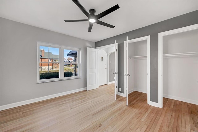 unfurnished bedroom featuring ceiling fan, light hardwood / wood-style floors, and multiple closets