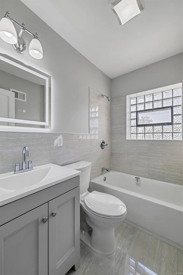 full bathroom with tiled shower / bath, vanity, toilet, and tile walls