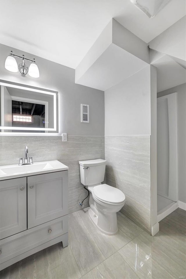 bathroom featuring walk in shower, vanity, toilet, and tile walls