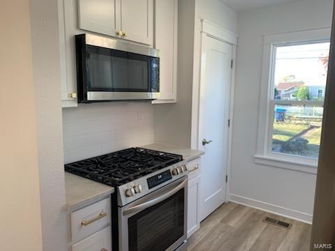 kitchen featuring white cabinets, backsplash, stainless steel appliances, and light hardwood / wood-style flooring