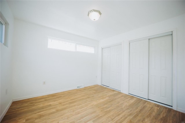 unfurnished bedroom featuring hardwood / wood-style floors and two closets