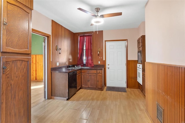 kitchen featuring ceiling fan, black dishwasher, light hardwood / wood-style flooring, wood walls, and oven