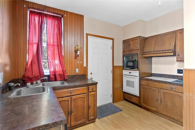 kitchen with black microwave, sink, white oven, cooktop, and light wood-type flooring