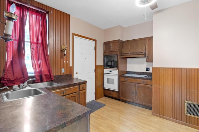 kitchen with black microwave, sink, cooktop, light hardwood / wood-style flooring, and oven