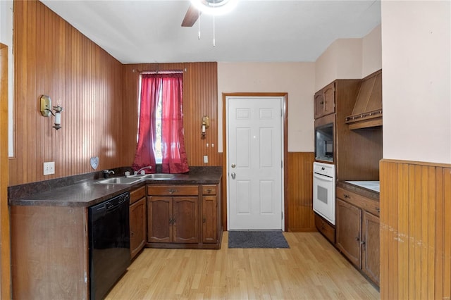 kitchen with wood walls, custom exhaust hood, black appliances, and light hardwood / wood-style floors