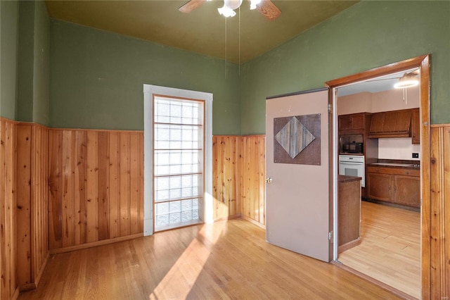 spare room with ceiling fan, wood walls, and light wood-type flooring