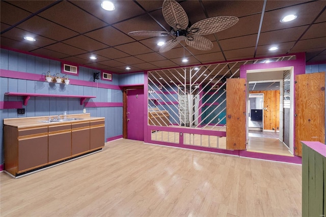 bar featuring light hardwood / wood-style floors, ceiling fan, wood walls, and sink