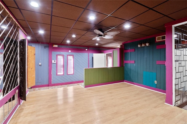 unfurnished room featuring a drop ceiling, hardwood / wood-style flooring, ceiling fan, and wood walls