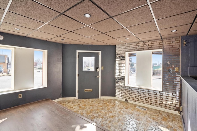 foyer entrance with a paneled ceiling and brick wall