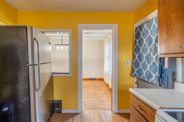 kitchen featuring decorative light fixtures, light hardwood / wood-style flooring, and stainless steel refrigerator