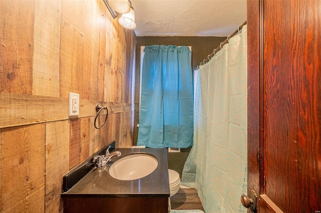 bathroom with a textured ceiling, vanity, toilet, and wooden walls