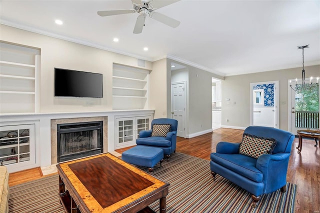 living room with hardwood / wood-style floors, ceiling fan with notable chandelier, crown molding, and built in shelves