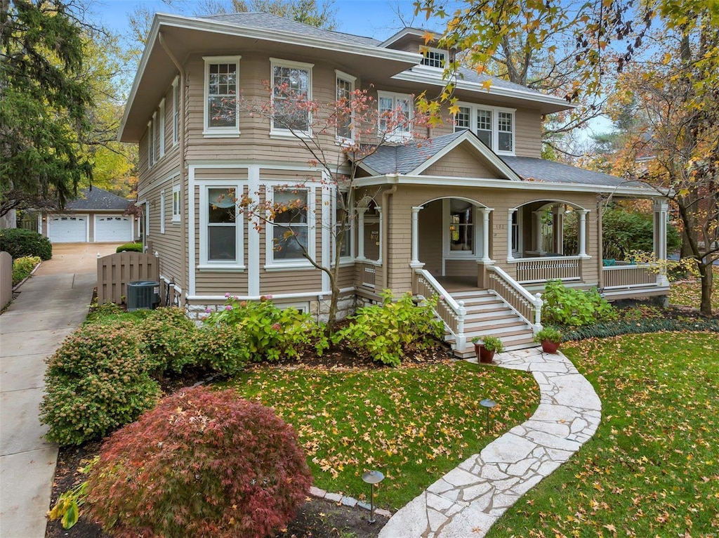 view of front of property with a front yard, a porch, cooling unit, a garage, and an outdoor structure