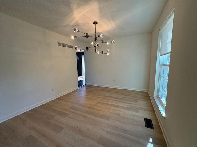 unfurnished dining area featuring a notable chandelier, light hardwood / wood-style floors, and a textured ceiling