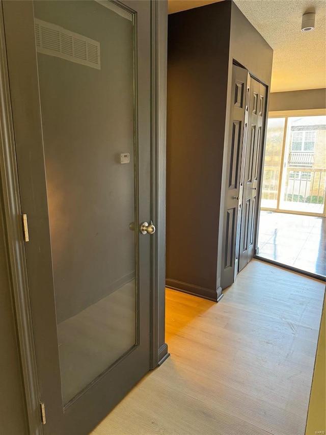 corridor featuring light wood-type flooring and a textured ceiling