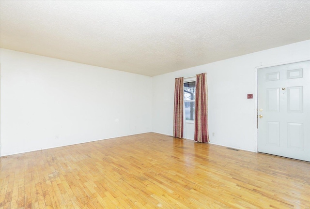 empty room with light wood-type flooring and a textured ceiling