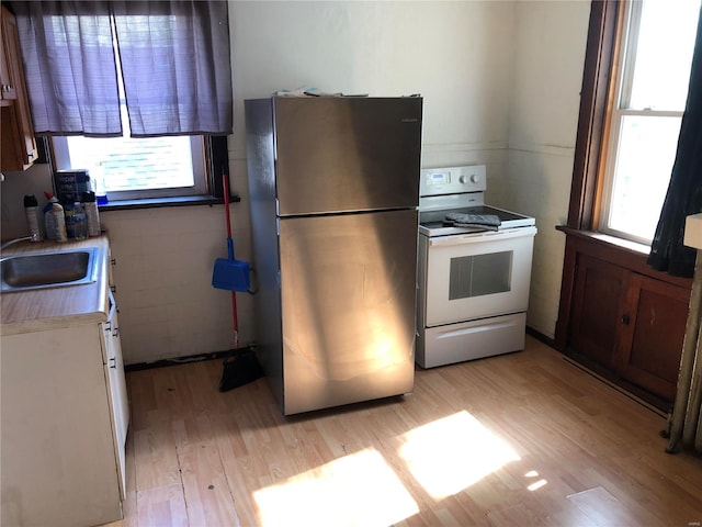 kitchen with white range with electric stovetop, stainless steel refrigerator, plenty of natural light, and light hardwood / wood-style flooring