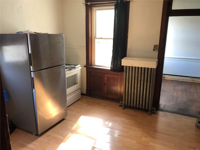 kitchen featuring light hardwood / wood-style floors, white range oven, radiator heating unit, and stainless steel refrigerator