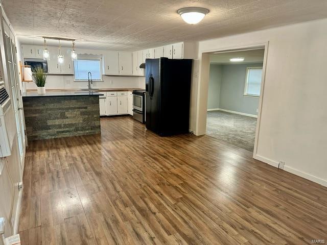 kitchen with white cabinets, dark hardwood / wood-style flooring, stainless steel range with electric stovetop, and black fridge