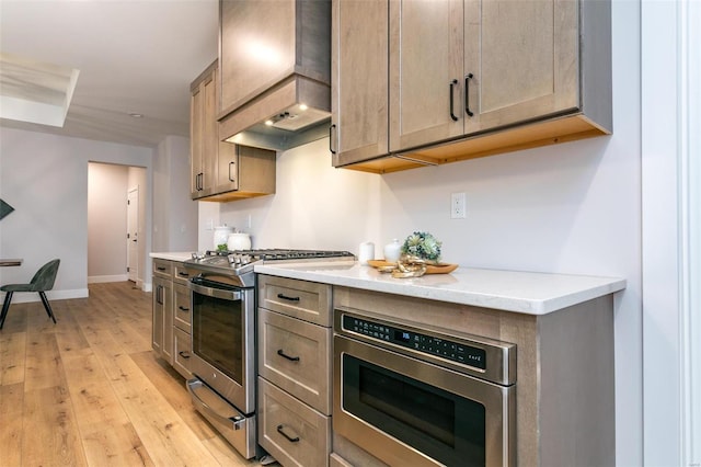 kitchen with light wood-type flooring, light stone counters, custom exhaust hood, and appliances with stainless steel finishes