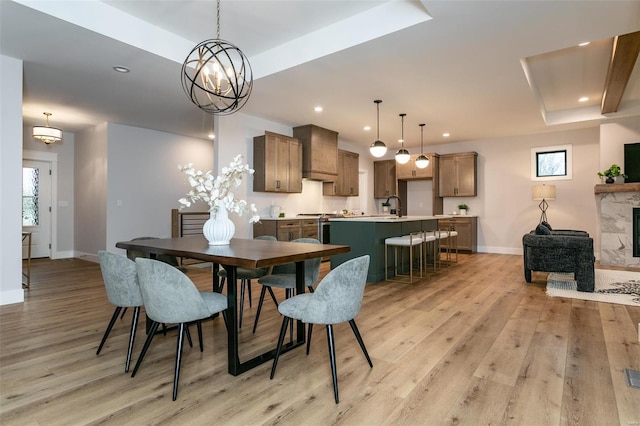 dining room featuring a fireplace, sink, a tray ceiling, and light hardwood / wood-style floors