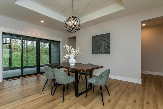 dining space featuring a raised ceiling, a chandelier, and light hardwood / wood-style floors