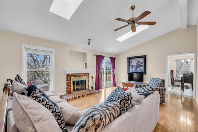 living room with a brick fireplace, ceiling fan, light wood-type flooring, and lofted ceiling with skylight