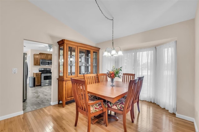 dining space with ceiling fan with notable chandelier, light wood-type flooring, and lofted ceiling