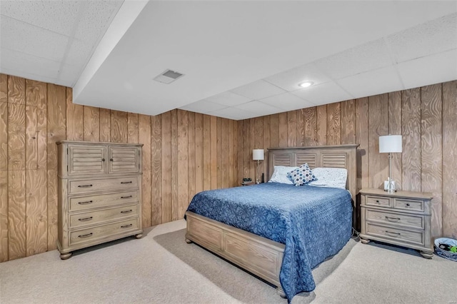 bedroom with a paneled ceiling, light colored carpet, and wooden walls