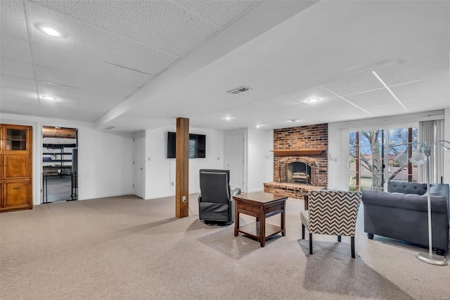 carpeted living room featuring a fireplace and a drop ceiling