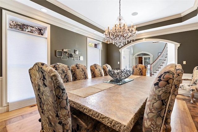 dining space with a raised ceiling, crown molding, and light hardwood / wood-style flooring