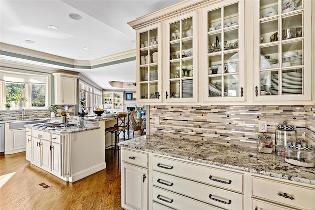 kitchen with tasteful backsplash, light stone counters, crown molding, and light hardwood / wood-style floors