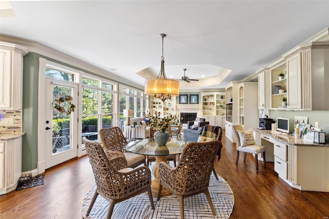 dining area featuring dark hardwood / wood-style floors, ceiling fan, ornamental molding, and a tray ceiling