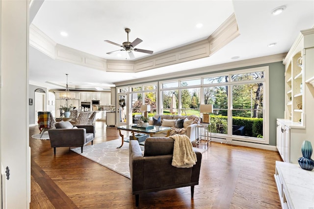 living room featuring a tray ceiling, crown molding, ceiling fan with notable chandelier, and hardwood / wood-style flooring