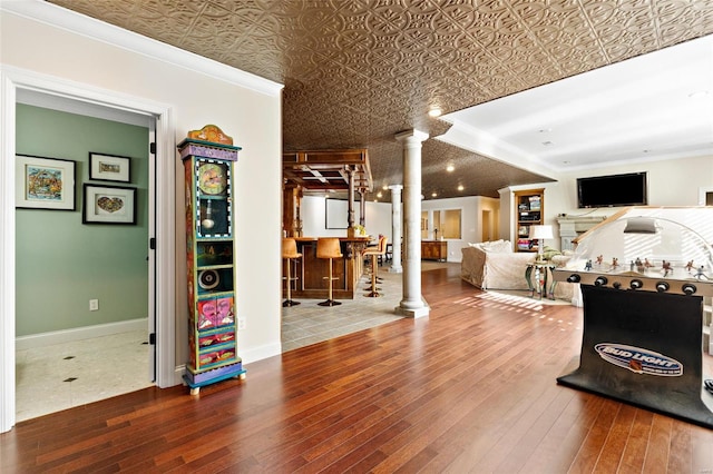 playroom featuring decorative columns, bar area, ornamental molding, and hardwood / wood-style flooring