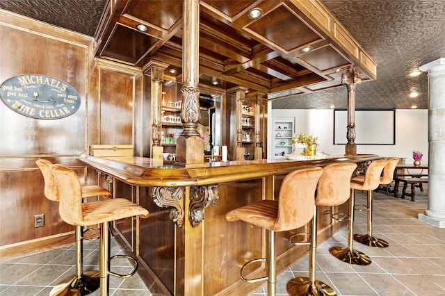 bar with decorative columns, tile patterned floors, coffered ceiling, beam ceiling, and wood walls