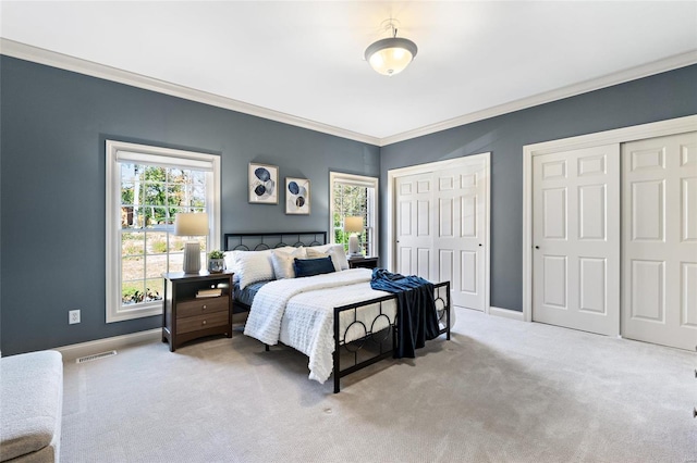 bedroom with two closets, light colored carpet, and crown molding