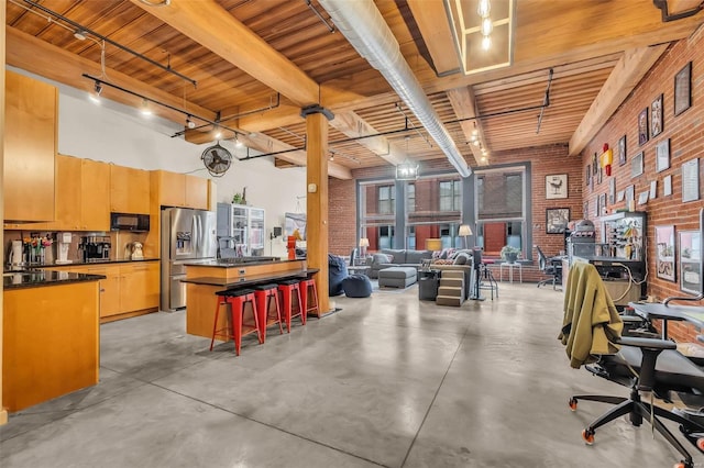 interior space with beam ceiling, a kitchen island, stainless steel refrigerator with ice dispenser, and brick wall