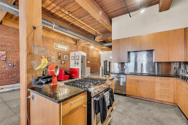 kitchen with dark stone counters, sink, light brown cabinetry, stainless steel appliances, and brick wall