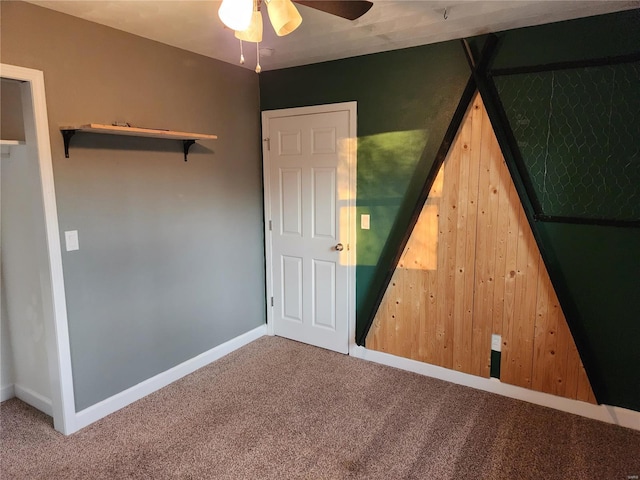 unfurnished bedroom with carpet floors, ceiling fan, and wooden walls