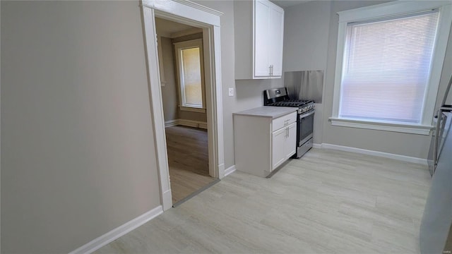 kitchen with light wood-type flooring, white cabinetry, a healthy amount of sunlight, and stainless steel range with gas stovetop