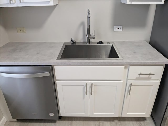 kitchen with white cabinets, light wood-type flooring, stainless steel dishwasher, and sink