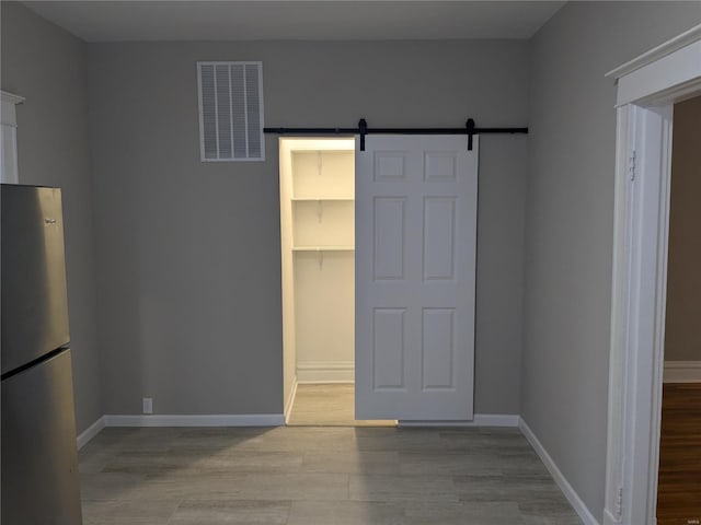 interior space with stainless steel fridge, a barn door, a spacious closet, light wood-type flooring, and a closet